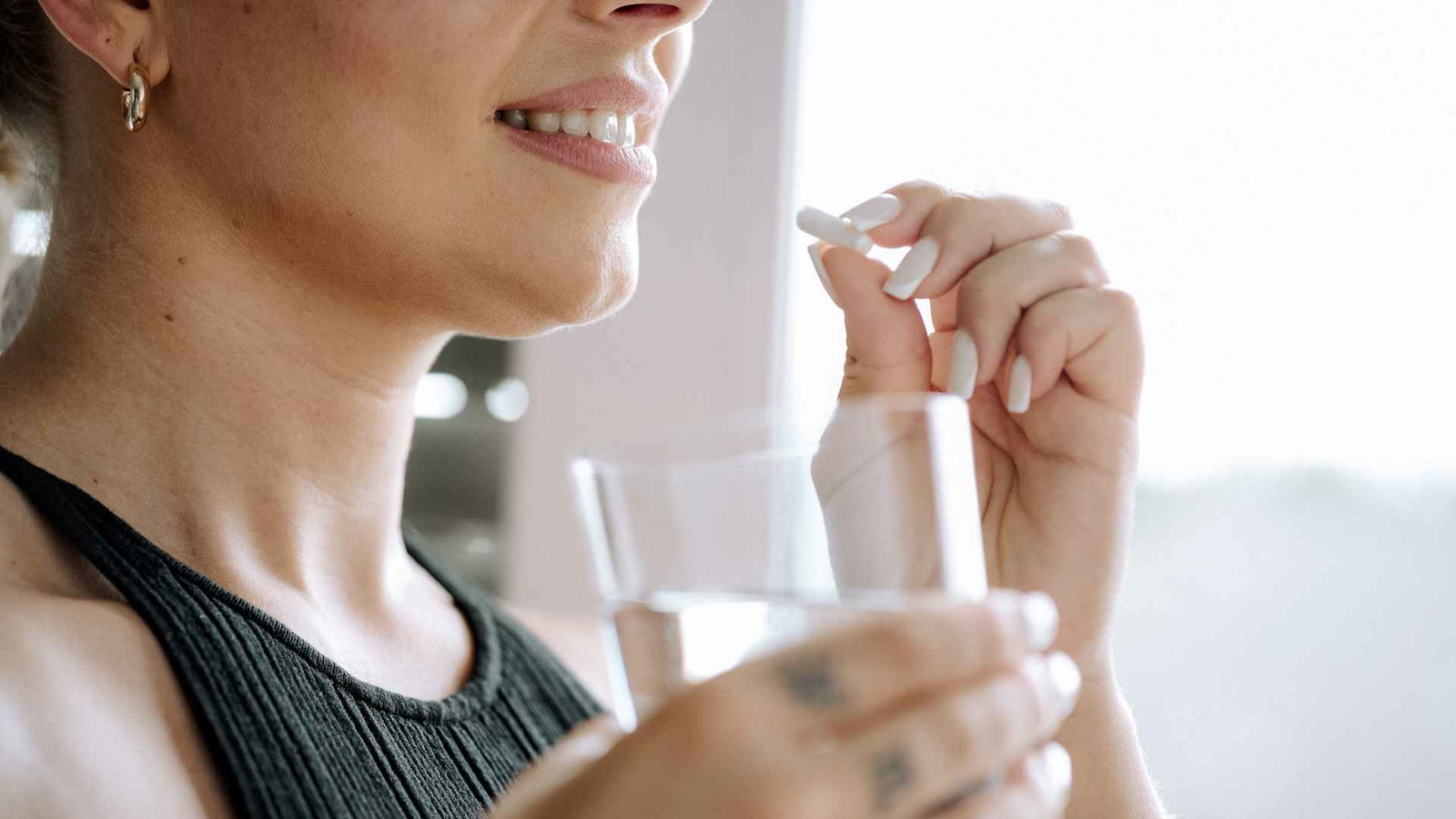 Frau nimmt eine weisse Tablette mit einem Glass Wasser