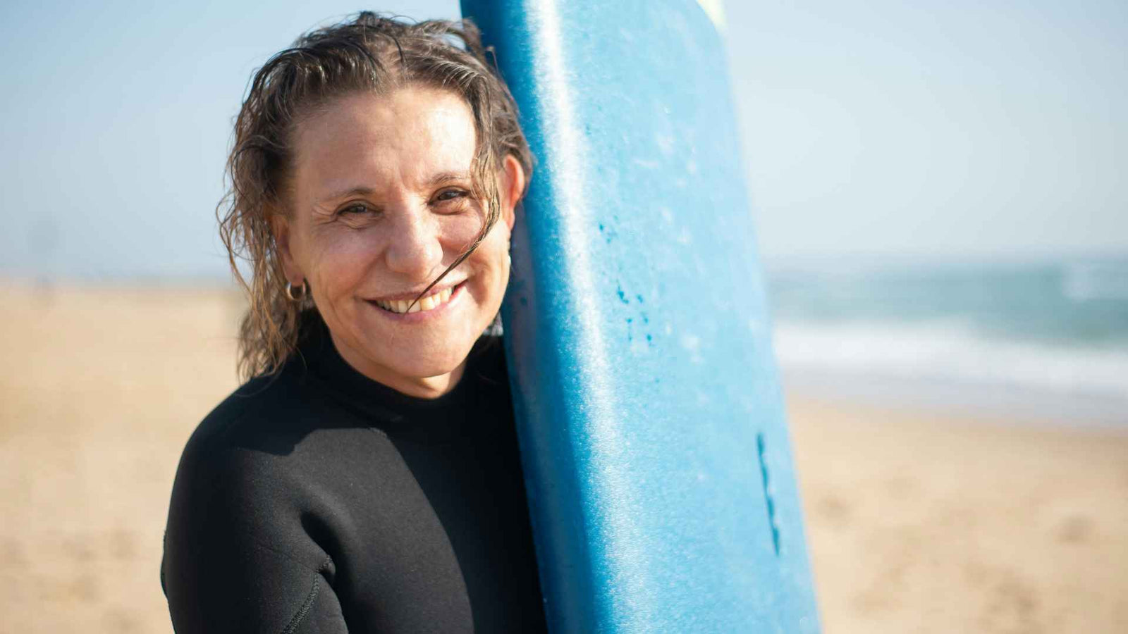 Frau mit aufgestelltem Surfbrett am Strand