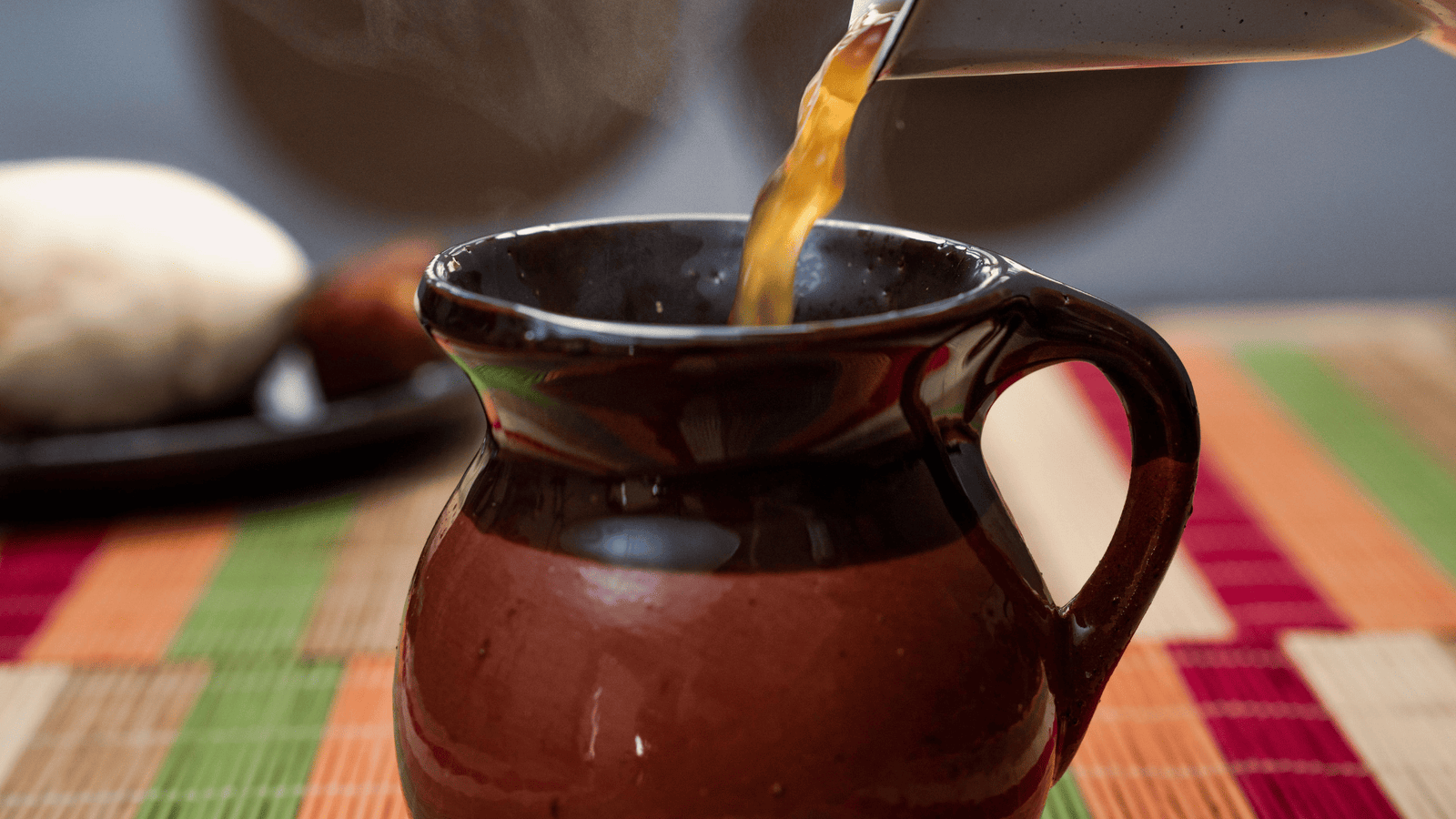 Krug auf Tisch, in den heisse Brühe gegossen wird. Bouillon selber machen ist nicht schwer.