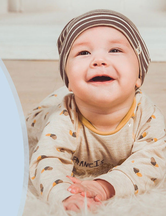 Lachendes, glückliches Baby auf dem Boden mit Mütze