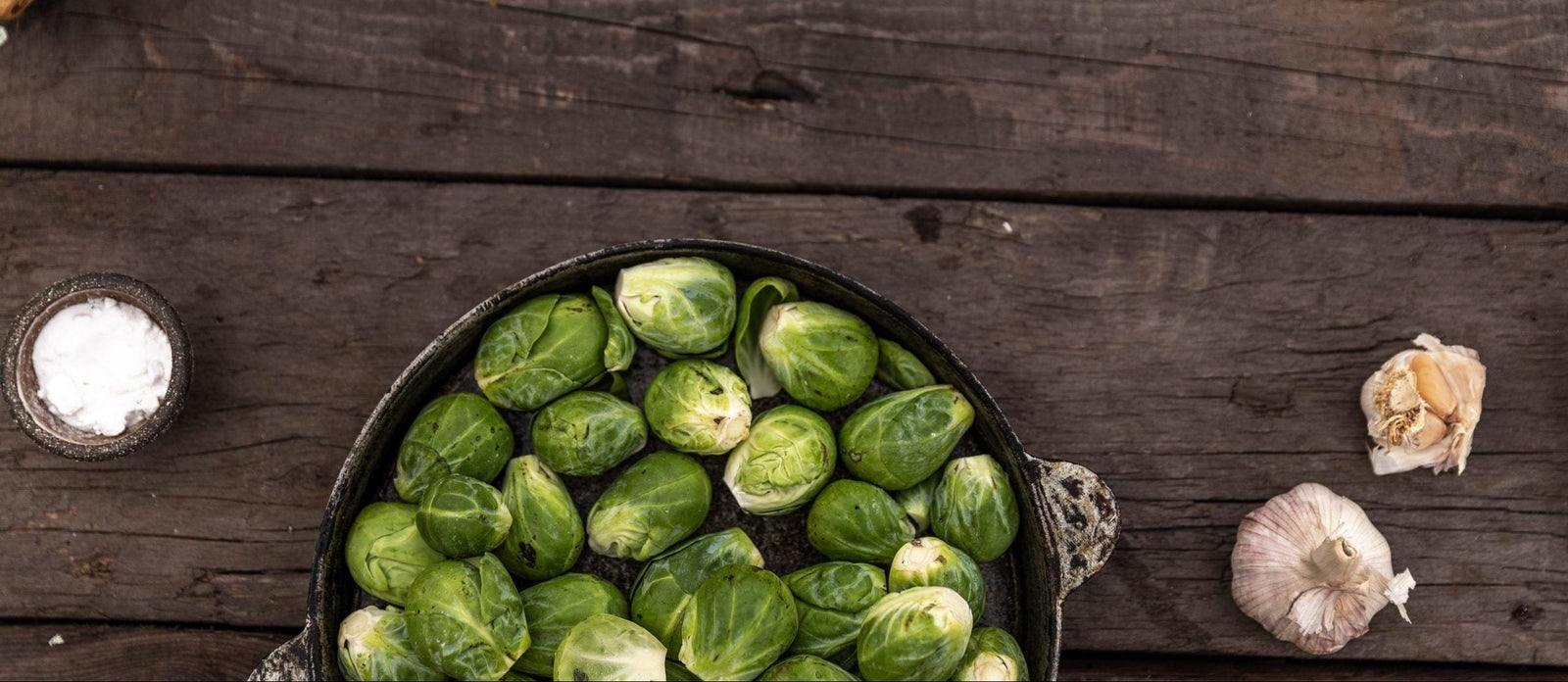 Essen und Gefühle: Rosenkohl in einer Schüssel auf einem Holztisch mit Knoblauch und Salz daneben platziert