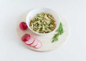 Radieschensalat, der Teil einer gesunden vegetarischen oder Veganer Ernährung sein kann, steht in einer Schlüssel auf einem mit Radieschen und Dill dekoriertem Brett.